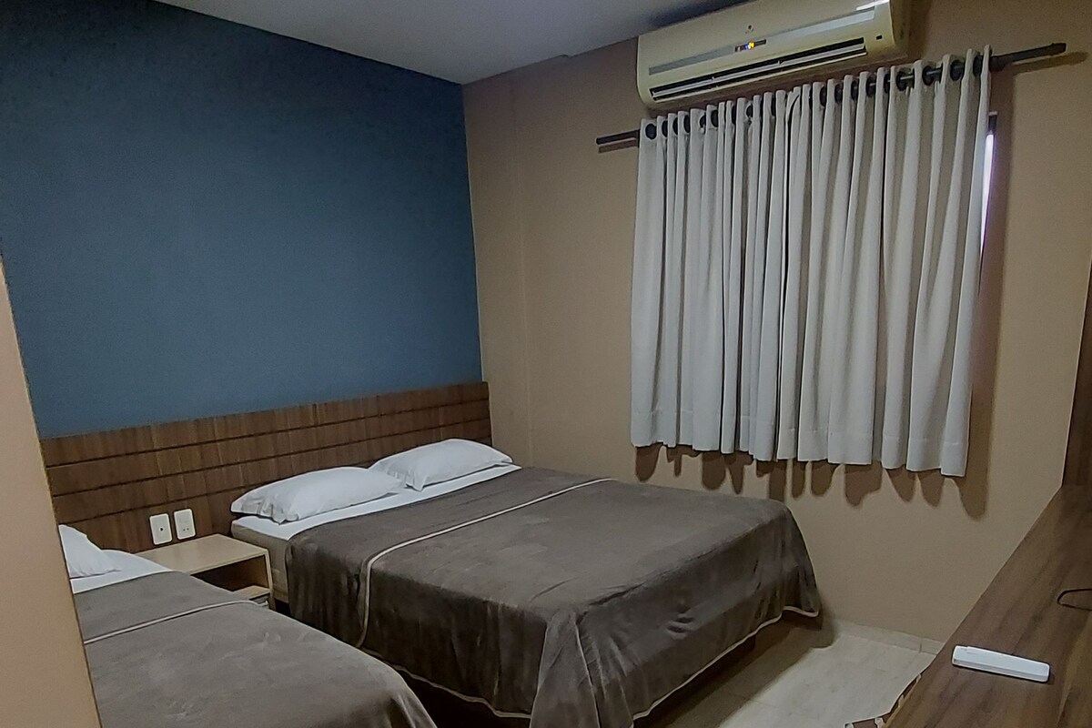A hotel room with two beds, a desk, an air conditioning unit, and a curtain.