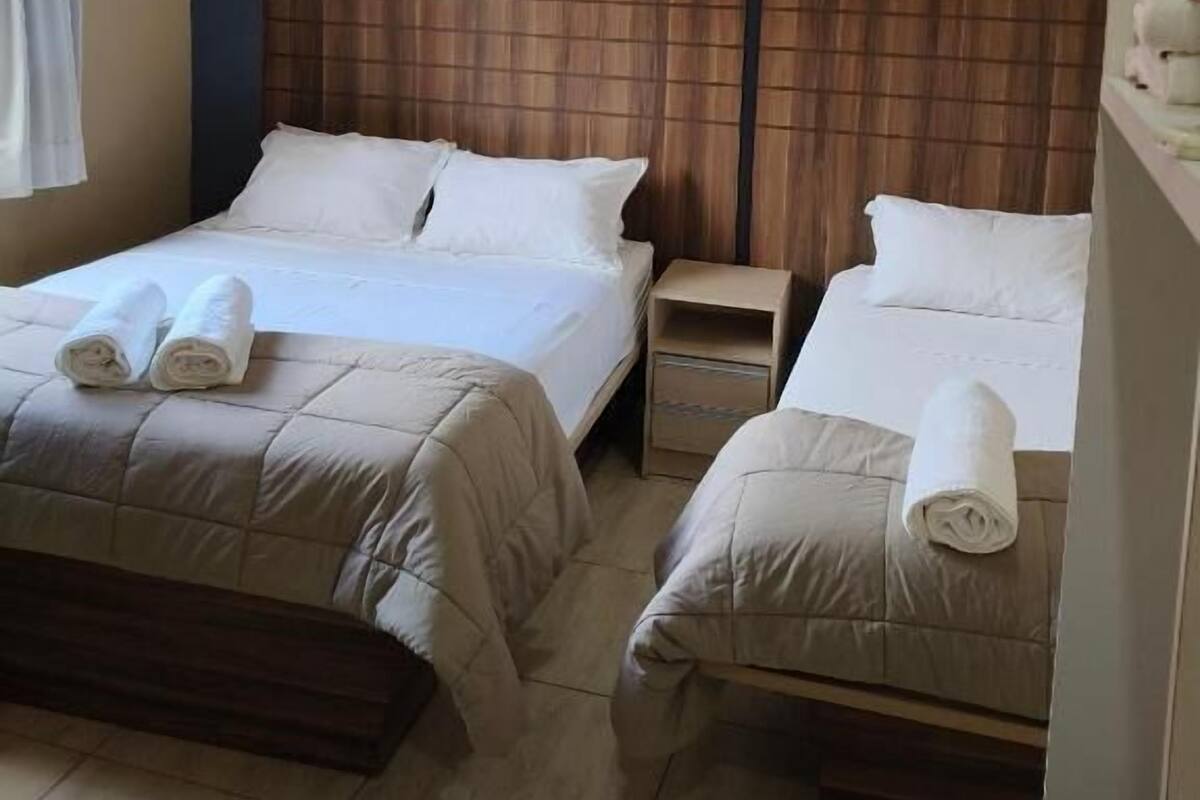 Ein Hotelzimmer mit zwei Betten, einem Deckenventilator, einem Nachttisch und einem Fenster mit Vorhängen.