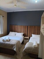 Habitación de hotel con dos camas, un ventilador de techo, una mesita de noche y una ventana con cortinas.