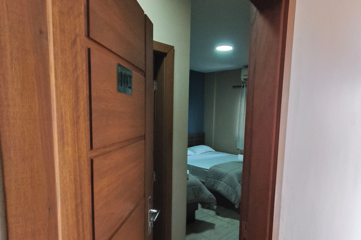 A wooden door with a number plate, leading into a room with a bed and a bedside table.