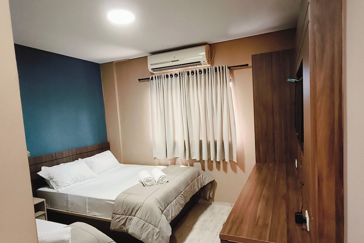 A hotel room with a bed, a sofa, a wooden cabinet, and an air conditioning unit.