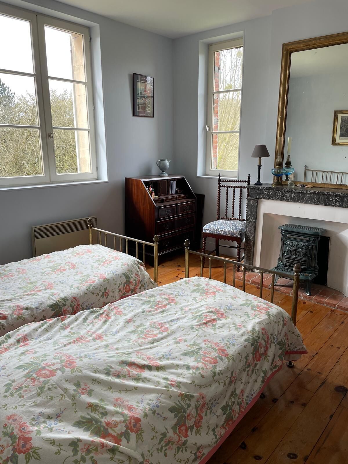 A room with two beds, a dresser, a chair, a fireplace, and a large mirror.