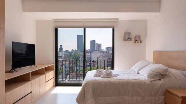Une chambre moderne avec vue sur la ville, un téléviseur à écran plat, un lit avec une literie blanche et une table de chevet en bois.