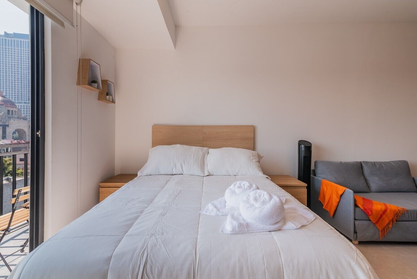 Een hotelkamer met een groot bed, een grijze bank en uitzicht op gebouwen.