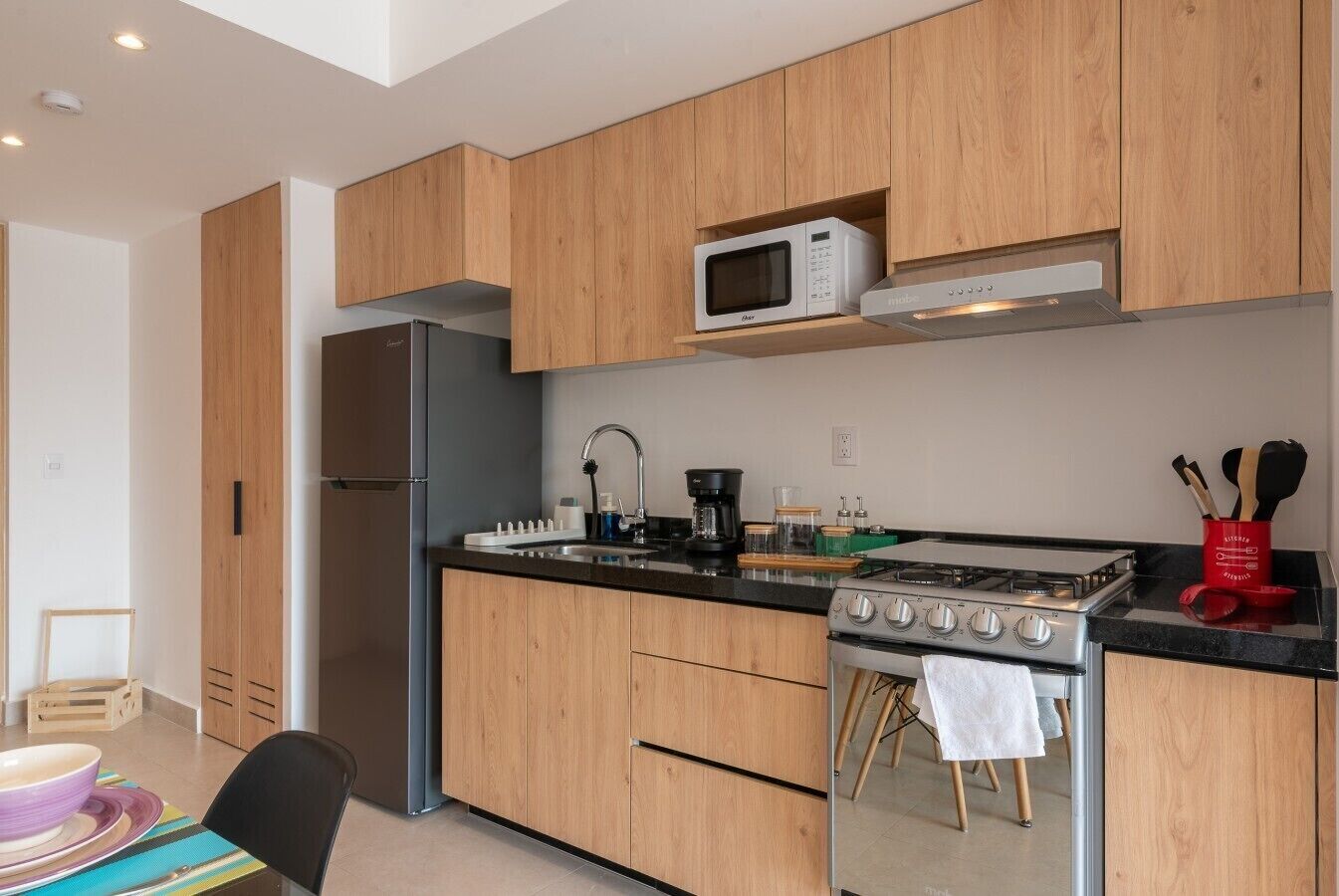 A modern kitchen with wooden cabinets, a stainless steel refrigerator, a microwave, a gas stove, and a sink.