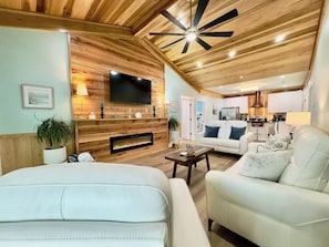 A modern living room with a fireplace, a television, and a ceiling fan.