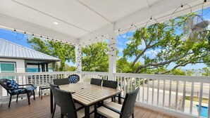 Eine überdachte Terrasse im Freien mit einem Holztisch und -stühlen, umgeben von einem weißen Geländer.