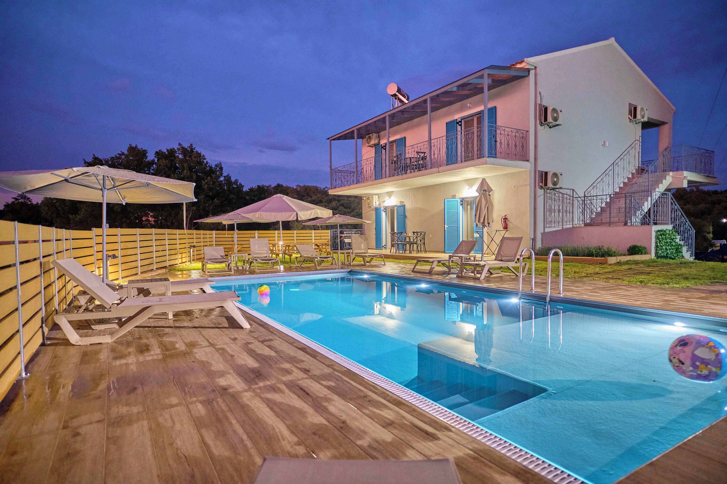 A swimming pool with lounge chairs and umbrellas, a two-story building with balconies, and a staircase.