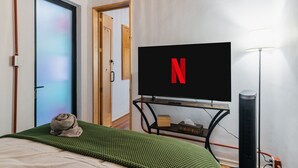 A room with a bed, a television displaying the Netflix logo, a lamp, and a door. - Stylish Roma Norte Loft | Walk to Cafés & Dining (Mexico City)