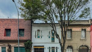A two-story building with a red-tiled roof, a large tree in front, and a gated entrance. - Stylish Roma Norte Loft | Walk to Cafés & Dining (Mexico City)