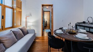 A modern living room with a sofa, dining table set for two, and a kitchen area with a sink and countertop. - Stylish Roma Norte Loft | Walk to Cafés & Dining (Mexico City)