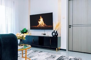 A modern living room with a flat-screen TV, a dark-colored entertainment unit, a glass coffee table, and a decorative vase with flowers. - Modern 1BR| Heated Pool, Gym, Fast Wifi| Kileleshwa (Nairobi)