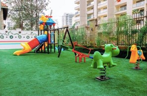 A playground with a slide, swings, and a climbing structure. - Modern 1BR| Heated Pool, Gym, Fast Wifi| Kileleshwa (Nairobi)