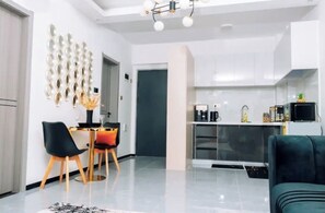 A modern kitchen with white cabinets, a dining area with black chairs, and a teal sofa. - Modern 1BR| Heated Pool, Gym, Fast Wifi| Kileleshwa (Nairobi)
