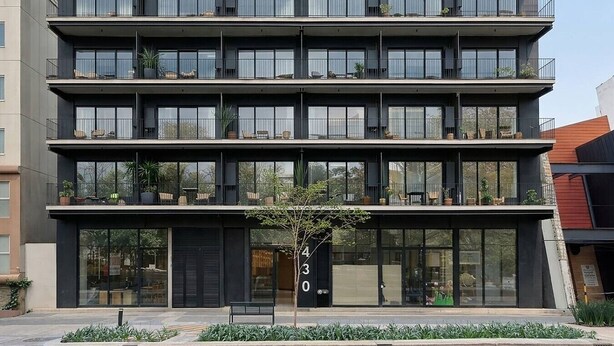 Un immeuble à plusieurs étages doté de balcons, de grandes fenêtres et d’espaces extérieurs aménagés pour s’asseoir.