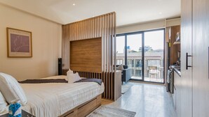 Une chambre d’hôtel moderne équipée d’un lit, d’une tête de lit en bois, d’un balcon avec vue et d’un coin cuisine.