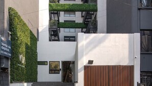 A modern building with a staircase leading to a gated entrance, a green vertical garden, and a sign indicating a sale. - City-Core Loft w/ Terrace + Rooftop Views (Mexico City)