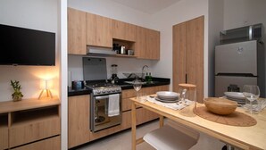 A modern kitchen with wooden cabinets, a stove, a refrigerator, and a dining table with glassware. - City-Core Loft w/ Terrace + Rooftop Views (Mexico City)