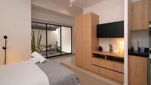 A modern bedroom with a bed, a TV, and a kitchenette. - City-Core Loft w/ Terrace + Rooftop Views (Mexico City)