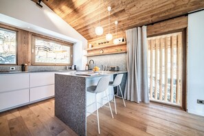 Eine moderne Küche mit einer zentralen Kochinsel, Barhocker, Pendelleuchten und einem großen Fenster.
