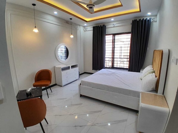 A modern bedroom with a bed, two chairs, a desk, a dresser, and a ceiling fan.