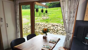 A dining area with a wooden table, chairs, a vase with flowers, and a view of a garden through a glass door. - VroniChalets - Tiny Chalet with sauna (Neukirchen)