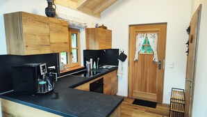 A kitchen with wooden cabinets, a black countertop, and a wooden door with a curtain. - VroniChalets - Tiny Chalet with sauna (Neukirchen)
