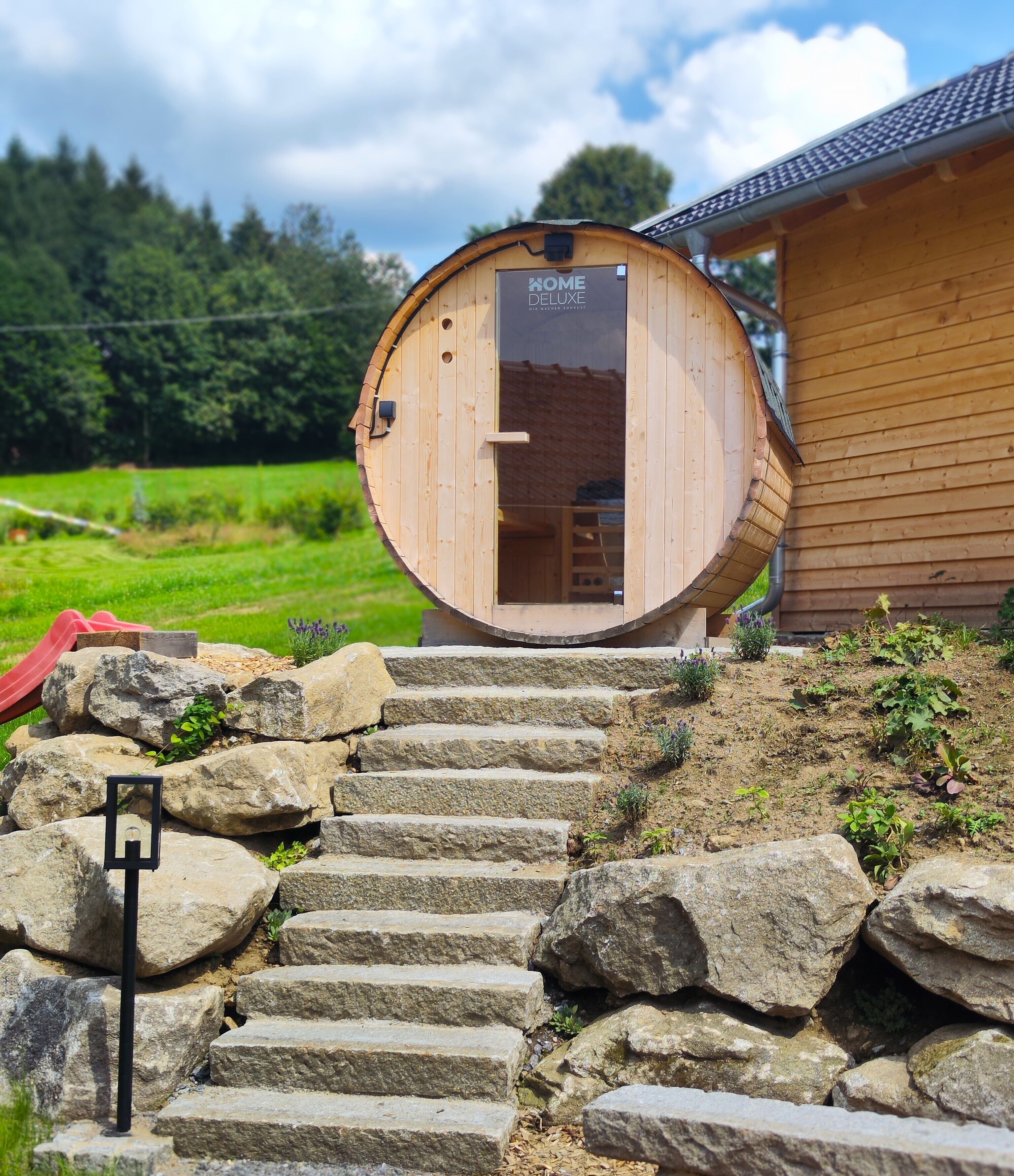 Une structure en bois sur laquelle est apposée une enseigne indiquant « KOME DELUXE », et un escalier en pierre menant à cette structure.
