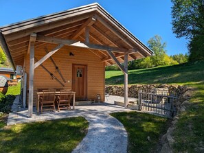 A wooden cabin with a covered porch, a door, and a bench. - VroniChalets - Tiny Chalet with sauna (Neukirchen)