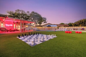 A poolside area with a checkered game board, lounge chairs, and a neon sign.