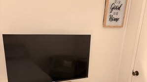 Una camera da letto con un letto, una TV su un supporto in legno, una piccola scrivania con cassetti, un termosifone e una citazione motivazionale sulla parete.