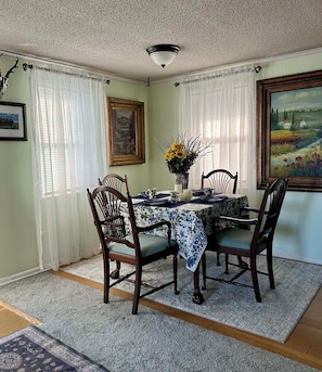 A dining room with a table set for four, surrounded by wooden chairs, a vase with flowers, and framed artwork on the walls.