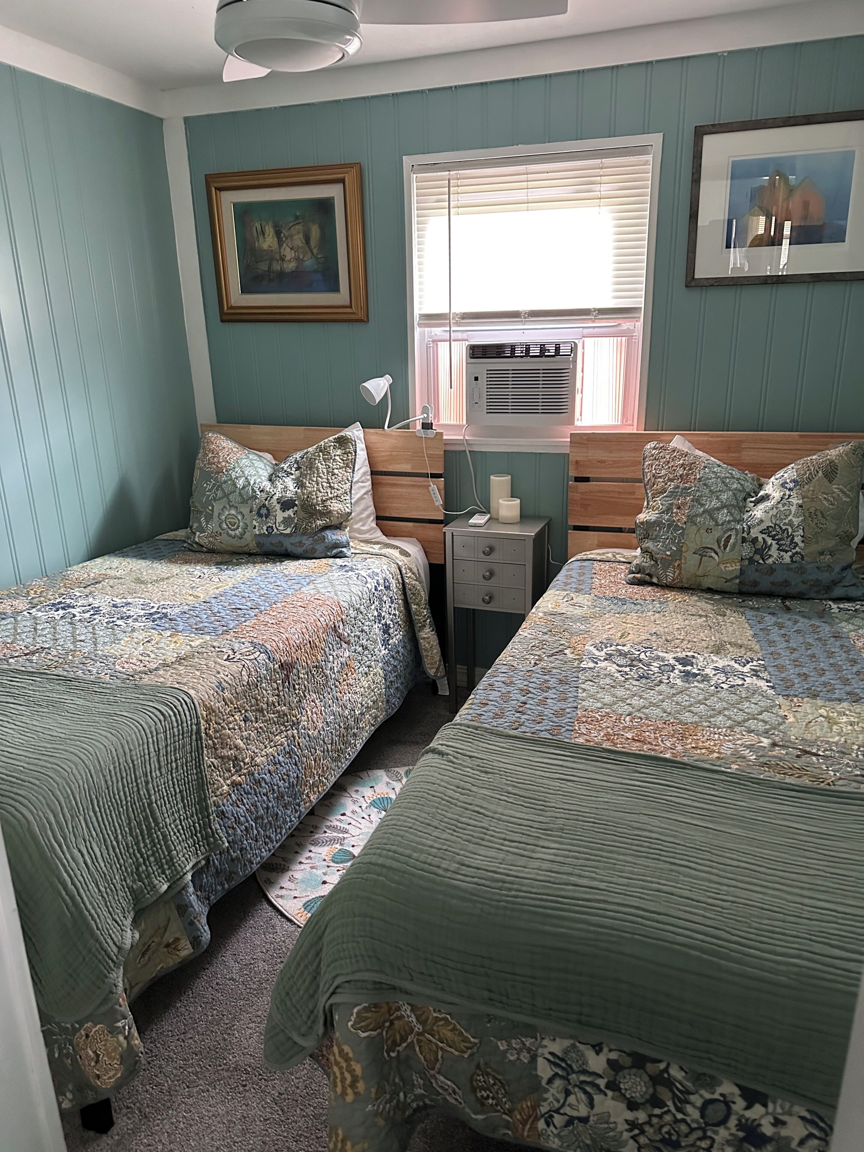 A bedroom with two beds, a nightstand, a lamp, and a window with blinds.
