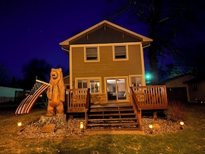 Une maison à deux étages avec une terrasse à l’avant, un escalier en bois et une statue d’ours.