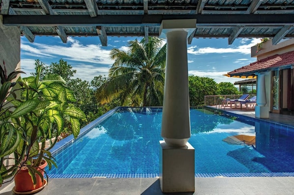 A clear blue pool with a stone column in the center, surrounded by lush greenery and a clear sky.