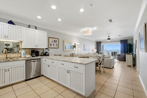 A modern kitchen with white cabinetry, a central island, and a dining area with a view. - Marlin Key 2D (Orange Beach)