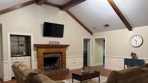 A living room with a fireplace, a television, and a clock on the wall. - Beautiful 4-bedroom house in tranquil Jackson perfect for families (Jackson)