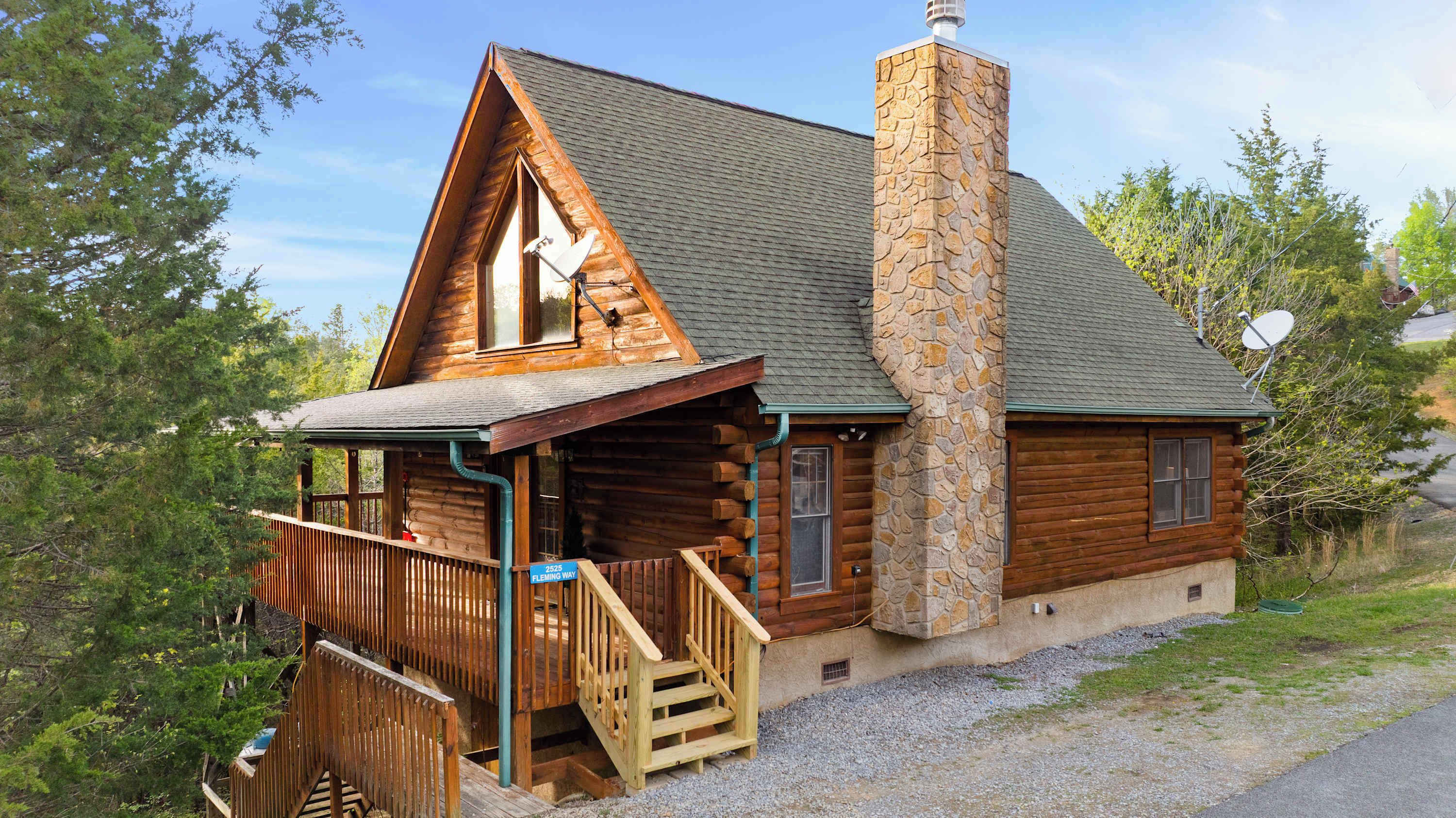 A log cabin with a stone chimney, wooden deck, and a staircase leading to the entrance.