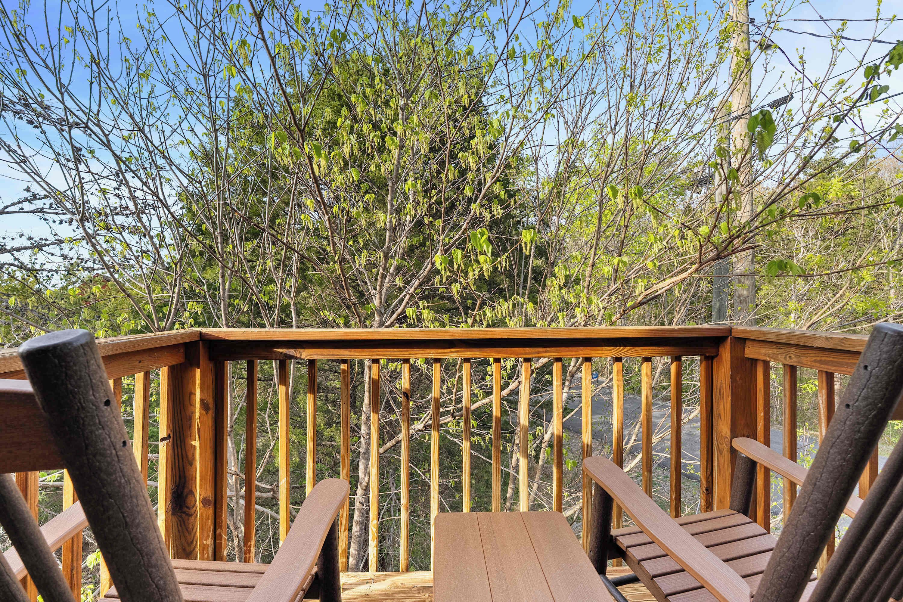 Eine Holzterrasse mit zwei Stühlen und einem Tisch, umgeben von Bäumen.