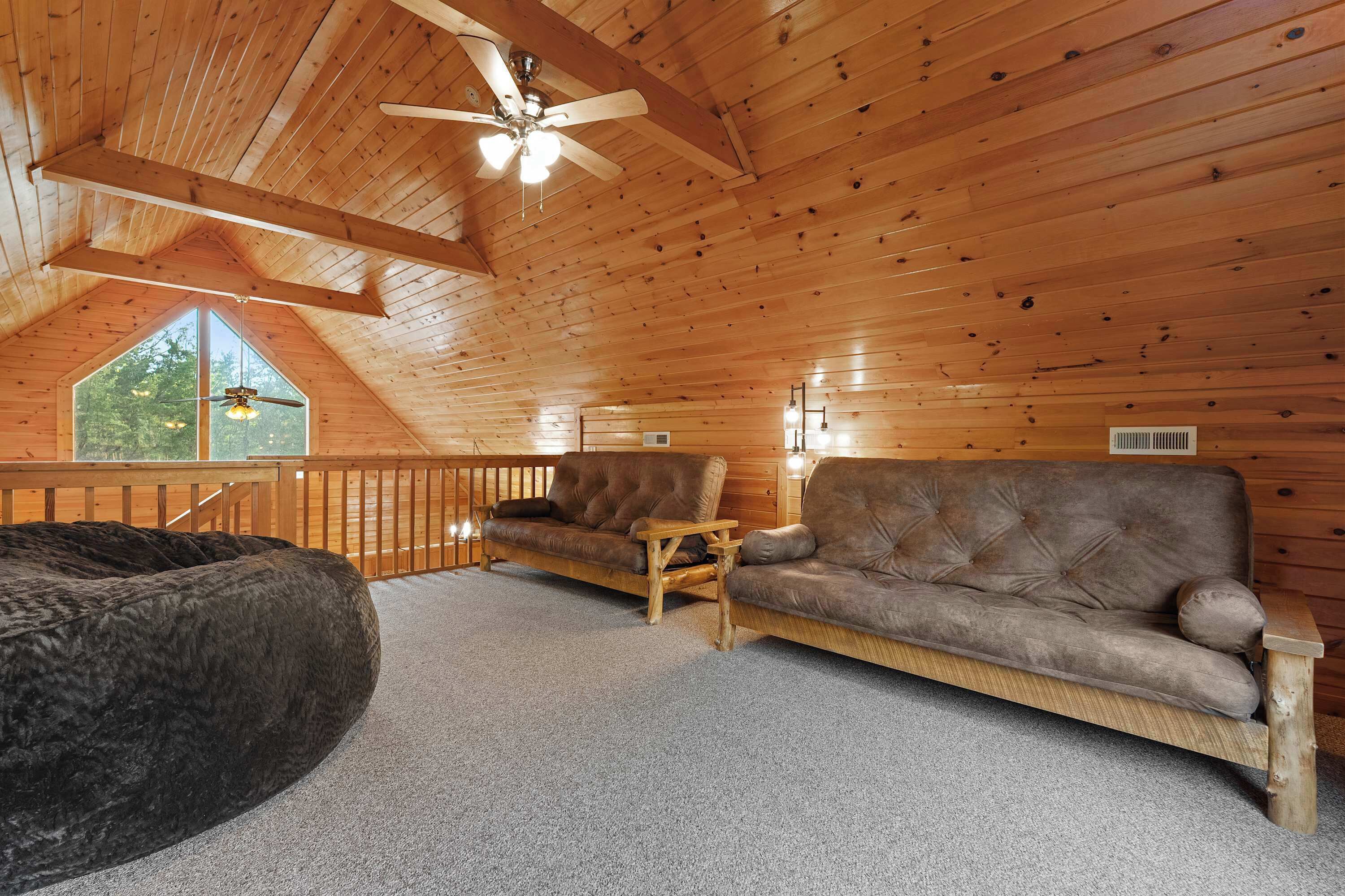 Un interior de madera con techo inclinado, un ventanal grande, un sofá de cuero marrón y un sillón informal.