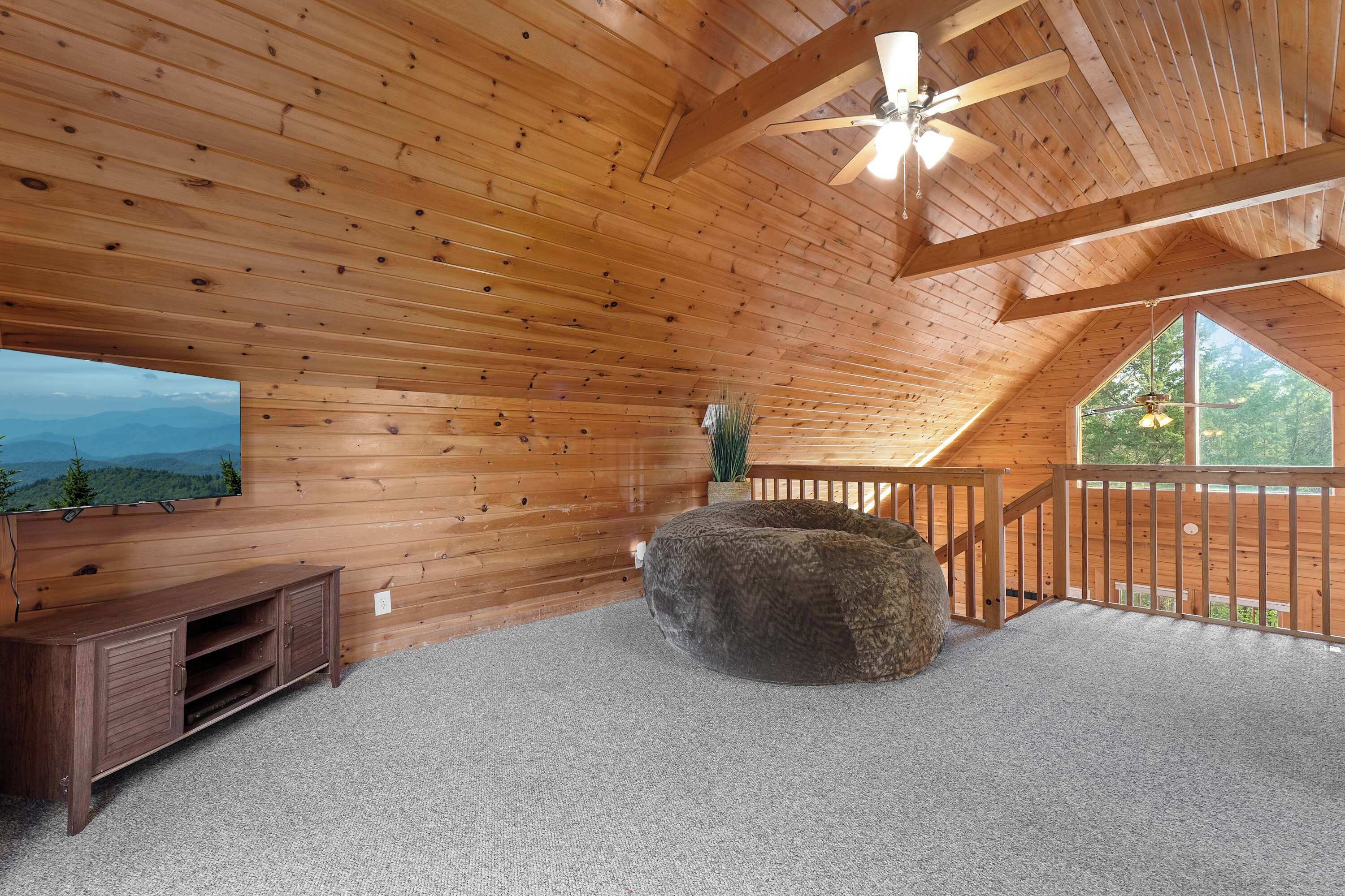 A wooden interior with a ceiling fan, a large window, a stone bench, and a TV on the wall.
