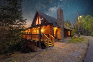 Ein Blockhaus mit einem Steinkamin, einer Holzterrasse und einer Veranda mit Stufen zu einem überdachten Bereich.