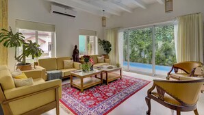 A spacious living room with a sofa, armchairs, a coffee table, and large windows offering a view of greenery.