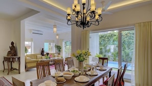 A dining area with a large table set for a meal, surrounded by chairs, with a chandelier above.