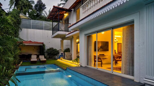 A swimming pool with a glass enclosure, a covered outdoor seating area, and a well-lit interior space.