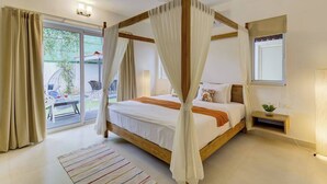 A bedroom with a four-poster canopy bed, a small bedside table with a plant, and a view of the outdoor area.