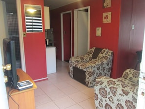 Una sala de estar con un sofá, una televisión y una cocina al fondo.