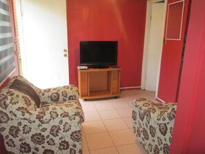 A room with a red wall, a television on a wooden stand, and two patterned sofas. - B1 Comfortable furnished 1-story apartment near downtown Puerto Montt (Puerto Montt)