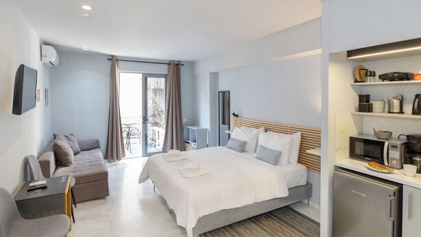 A modern hotel room with a bed, a sofa, a desk, a refrigerator, and a kitchenette.