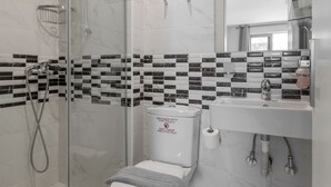 A bathroom with a glass-enclosed shower, a toilet, and a sink with a mirror above it.